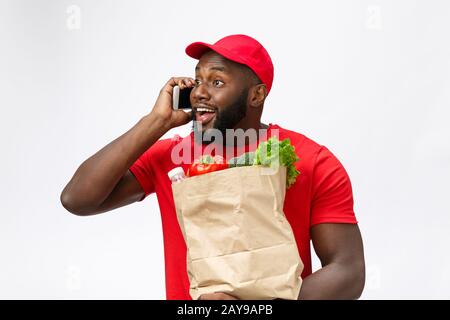 Concept de livraison - Portrait de L'Homme de livraison Afro-américain Ou de coursier avec paquet d'épicerie et parler sur le mobile phon Banque D'Images