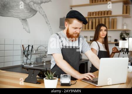 Coffee Business concept - Bartende barbu, barista ou responsable travaillant et planant sur un ordinateur portable dans un café moderne Banque D'Images