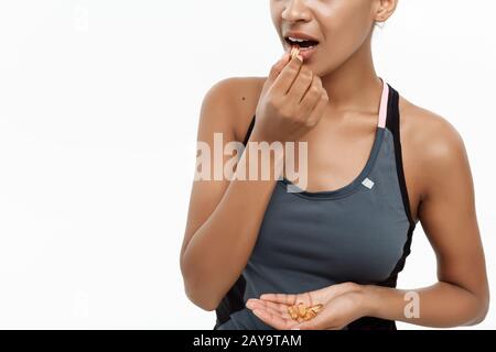 Concept de santé et de remise en forme - gros portrait de la belle afro-américaine prenant une pilule de l'huile de foie de morue. Isolé sur blanc s Banque D'Images