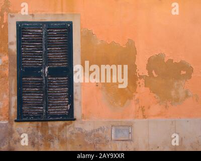 Une vieille fenêtre avec volets en bois fermés peints en vert sur un mur orange d'ocre méditerranéen Banque D'Images