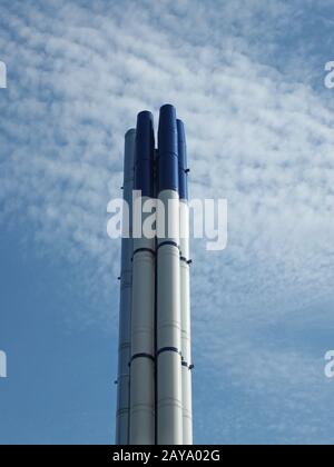 un groupe de grands cheminées industrielles en acier moderne, debout contre un ciel bleu vif et des nuages blancs Banque D'Images