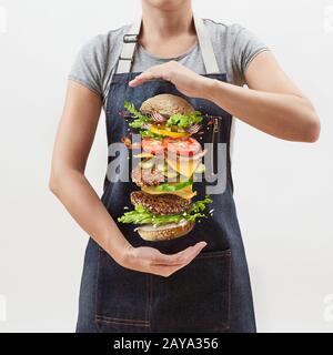 Gros hamburger frais maison dans les mains de la fille à partir d'ingrédients volants - légumes frais et viande de boeuf naturelle biologique sur une merde Banque D'Images