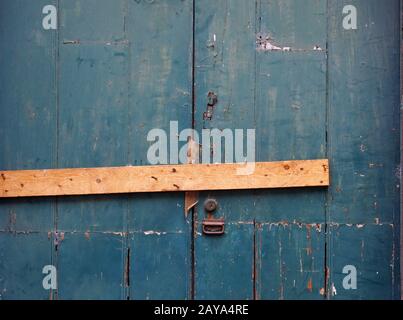 gros plan d'une vieille porte en bois peinte vert décolé barré fermé avec un morceau de bois et des clous rouillés avec une serrure et ha Banque D'Images