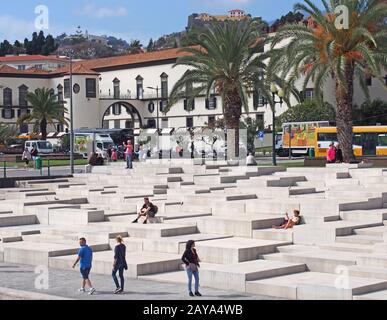 touristes assis et passants sur les marches en béton de la marina de funchal face à la vieille ville Banque D'Images