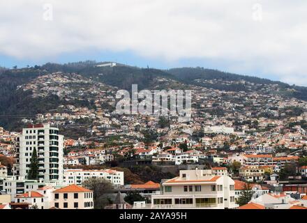 vue sur la ville de funchal à madère montrant des bâtiments blancs en face des montagnes couvertes de forêt avec des nuages blancs au-dessus Banque D'Images