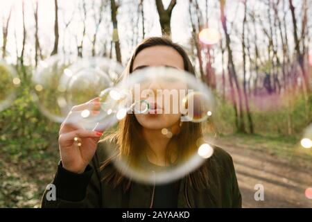 Jeune femme soufflant des bulles de savon dans les bois. Liberté, style de vie et concept de mise en réseau. Coloré v Banque D'Images