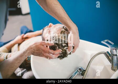 Thème du barbershop. Coiffeur pour laver les cheveux dans un barbershop. Mains hommes coiffeur gros-up lave les cheveux avec mousse et shampo Banque D'Images