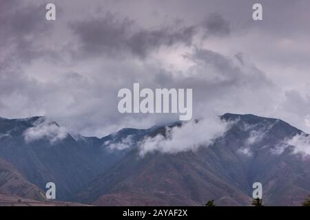 Lahaina, Maui, Hawaï, États-Unis. - 12 janvier 2012: Les nuages gris contre le ciel argenté se balader au-dessus de la chaîne de montagnes du volcan Haleakala brun noir. Banque D'Images