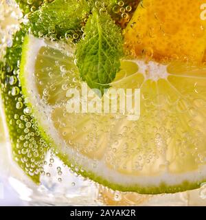 Macro photo de tranches de lime vert, jaune citron et feuille de menthe avec des bulles dans un verre. Cocktail d'été Banque D'Images