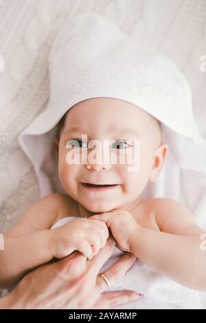 beau bébé souriant garçon couvert avec une serviette en bambou blanc avec des oreilles amusantes. se trouve sur une maille blanche, laine plaid brillant interi Banque D'Images