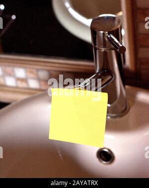 Papier à note rectangulaire jaune fixé sur le robinet de l'évier de toilettes. Pièce de feuille carrée utilisée pour donner la notation coller au robinet d'eau en t Banque D'Images