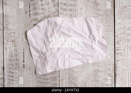 Papier déchiré froissé placé au-dessus d'une table en bois. La feuille demi-cassée s'adhère à l'arrière-plan classique en position inclinée. Façon artistique Banque D'Images