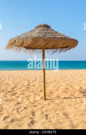 Un parasol de plage en osier sur la côte avec mer bleue Banque D'Images