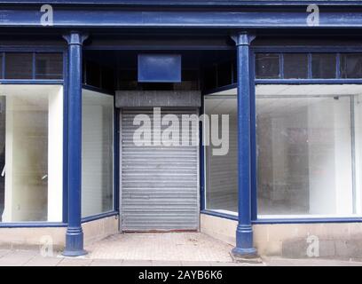 la façade d'un vieux magasin abandonné a peint bleu et blanc avec des fenêtres sales vides devant le magasin et des volets fermés sur la porte Banque D'Images