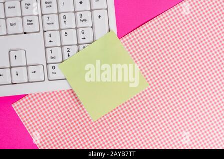 Note feuille collée sur le clavier de l'ordinateur près de tissu à motifs au-dessus d'une table colorée. Outil de traitement de données placé bel Banque D'Images