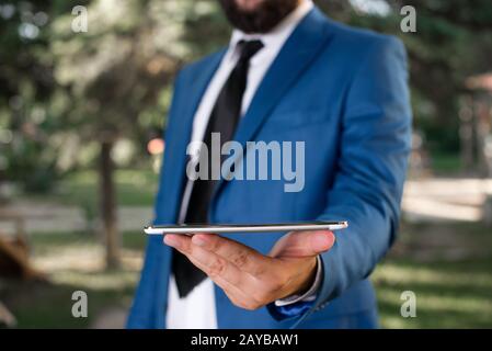 Concept d'entreprise avec un homme tenant un téléphone mobile avec écran tactile. Homme d'affaires tient le dessus de tour dans sa main. Homme d'affaires en bleu sui Banque D'Images