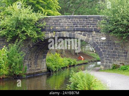 un vieux pont en pierre traversant le canal de rochdale à mytholmroyd west yorkshire avec une allée côté eau entourée d'arbres et b Banque D'Images