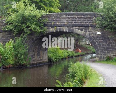 un vieux pont en pierre traversant le canal de rochdale à mytholmroyd west yorkshire avec une allée côté eau entourée d'arbres et b Banque D'Images