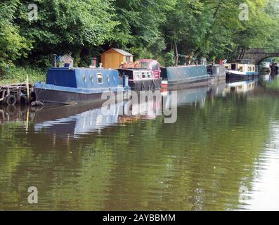 des bateaux étroits et des barges amarrés sur le canal de rochdale dans le pont de hebden, entourés d'arbres verts d'été et d'un pont en pierre Banque D'Images