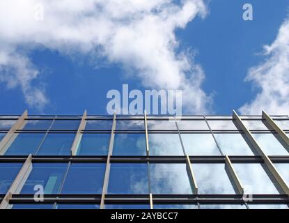 bâtiment moderne de bureau avec fenêtres en verre miroir reflétant un ciel bleu vif et des nuages blancs Banque D'Images