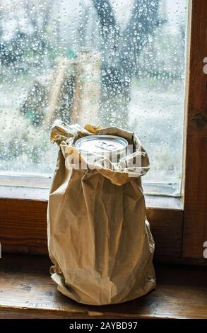 Bouteille d'alcool dans un paquet de papier brun placé à la fenêtre le jour de la pluie. Paquet de papier froissé. Banque D'Images