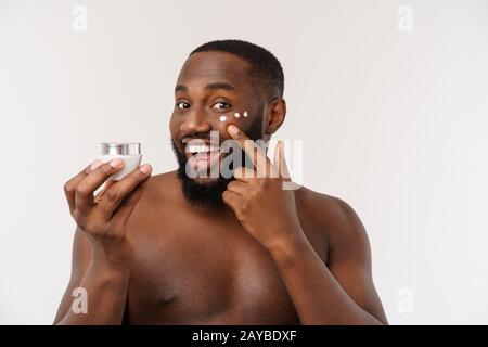 Smiling afro homme l'application de la crème sur son visage. Concept de soins de la peau de l'homme Banque D'Images