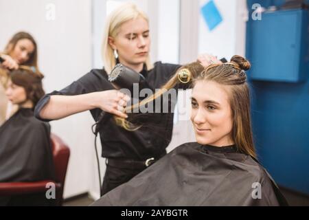 Portrait d'une femme heureuse au salon de coiffure. Concept professionnel de coiffure. Coiffeuse séchage fille cheveux longs avec sèche-cheveux Banque D'Images