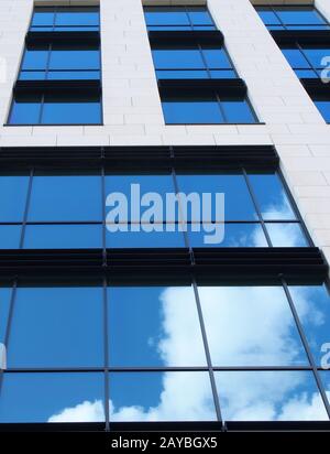 bâtiment moderne de bureau blanc avec fenêtres en verre miroir reflétant un ciel bleu vif et des nuages blancs Banque D'Images