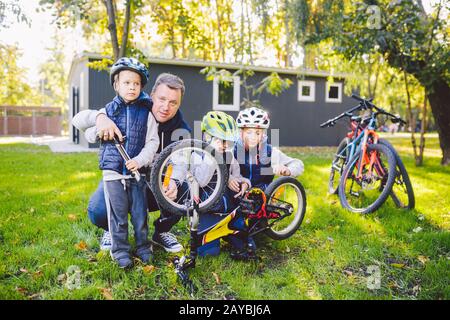 Fête des pères un grand père de famille sympathique et trois fils conjoints de repos actif dehors. Papa enseigne aux fils de réparer le vélo. Le chil Banque D'Images