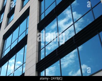 vue angulaire d'un bâtiment commercial moderne avec de grandes fenêtres en miroir reflétant le ciel bleu et les nuages blancs Banque D'Images