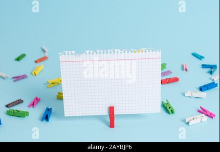 Papier coloré en forme de clothespin et rectangulaire en forme de carré sur fond bleu. Clip rouge accrochant un rappel de note dans un espace vide Banque D'Images