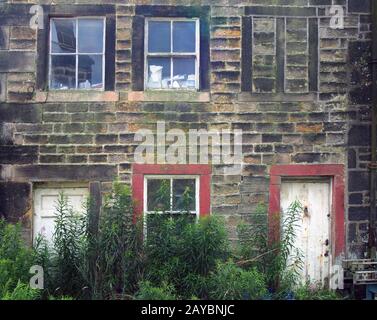 les vieilles maisons désertes sont délabrées avec de la peinture écaillée et des murs fissurés en décomposition avec l'avant surcultivé avec des mauvaises herbes Banque D'Images