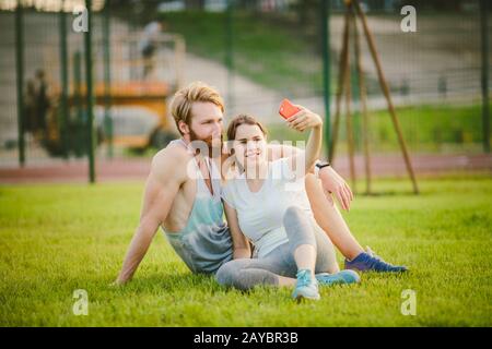 Sport et technologie. Jeune en amour couple hétérosexuel caucasien se reposant après l'entraînement en plein air dans le parc sur pelouse, herbe verte si Banque D'Images