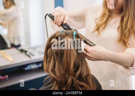 beauté, coiffure concept, heureuse jeune femme et coiffeuse avec fer à repasser coiffure coiffure coiffure au salon de coiffure. Femme Ayant Des Cheveux Styli Banque D'Images