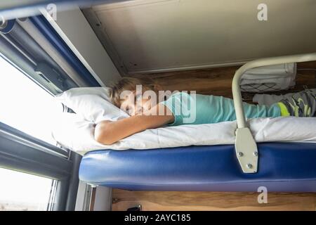 Une fillette de huit ans se trouve sur l'étagère du haut d'un siège réservé voiture et a l'air fatigué par la fenêtre Banque D'Images