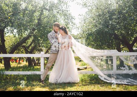 Couple caucasien dans l'amour de la mariée et de la groom debout dans embrasser près de bois blanc, clôture rurale dans le parc un verger de pomme. Thème est W Banque D'Images