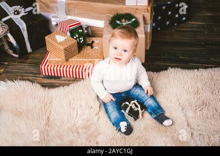Thème hiver et Noël vacances. Enfant garçon caucasien blond 1 an assis à l'étage près de l'arbre de Noël avec le nouvel an d Banque D'Images