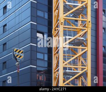 gros plan sur la tour d'une grue de construction jaune avec échelles en acier soulevant un crochet avec chaîne contre un bâtiment noir moderne Banque D'Images