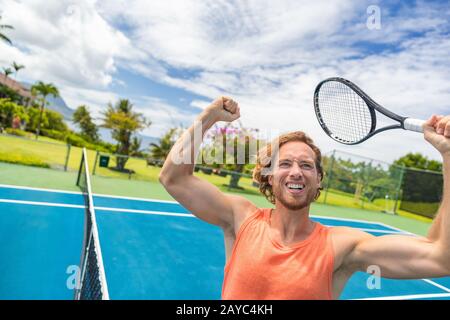 Joueur de tennis man cheering gagnante célébrant la victoire. Homme heureux gagnant dans la célébration du succès et de la victoire. Mettre en place sur l'athlète masculin de tennis en plein air holding tennis racket en triomphe par le net. Banque D'Images