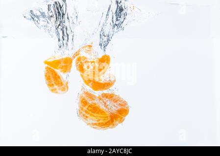 La baisse isolée d'orange dans l'eau. Morceaux de fruits orange pelées dans l'eau isolé sur fond blanc Banque D'Images