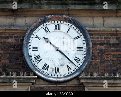 vieille horloge sur le mur de briques d'un bâtiment avec chiffres romains et visage épluché affligé avec les mains à vingt-dix Banque D'Images