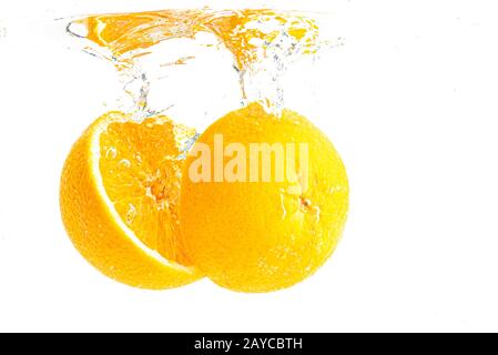 Orange organique tranché en deux temps s'enfonçant dans de l'eau cristalline avec des bulles d'air Banque D'Images