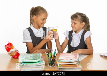 Deux écolières drôle à une table, boire du jus, et frappait verres Banque D'Images