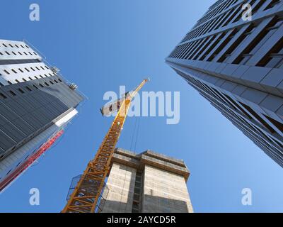 vue verticale d'une grande grue de construction jaune travaillant sur un nouveau bâtiment en béton avec un grand surr Banque D'Images