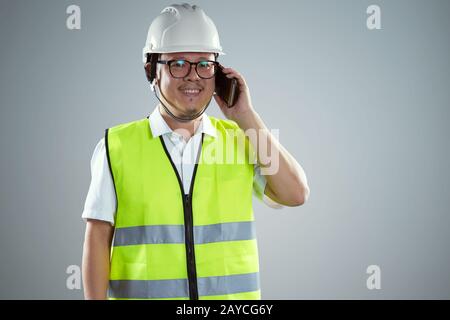 Portrait d'un jeune ingénieur asiatique confiant portant un casque de protection et utilisant un smartphone . Banque D'Images