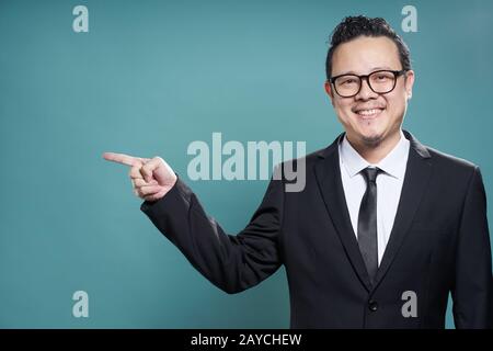 Portrait of asian businessman smile et des points avec le doigt à l'appareil photo à gauche sur fond bleu vintage . Banque D'Images