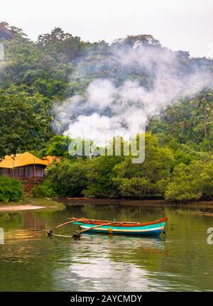 Région tropicale région côtière éloignée de la forêt de mangroves avec colline et nuages, un chalet temporaire et un canoë en bois pour l'aviron et la pêche dans l'étang Banque D'Images