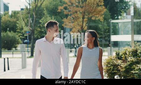 Les couples multiethniques se regardent en se promenant dans la rue, en tenant les mains et en parlant. Concept de relation. Banque D'Images