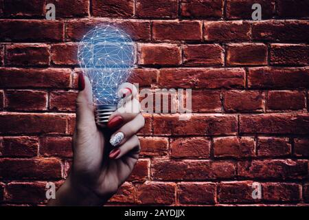 Femme tenant une ampoule sur un fond de mur de briques. Banque D'Images