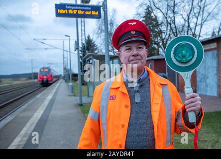 06 février 2020, Mecklembourg-Poméranie occidentale, Sülstorf: Le chauffeur de taxi de Berlin Michael Böhmke est debout sur la plate-forme devant la gare "HIS" de Sülstorf portant un chapeau de chemin de fer. En arrière-plan, le express régional des arrêts de la Deutsche Bahn. Il y a deux ans, Böhmke a acheté la gare sur la ligne de chemin de fer de Ludwigslust à Schwerin lors d'une vente aux enchères sur Ebay. Peu à peu, il veut maintenant étendre et rénover le bâtiment; il a déjà recueilli de nombreux éléments de collection relatifs à l'histoire ferroviaire. (À dpa ''C'est mon terrain de jeu' - stations entre la désintégration et le départ') Pho Banque D'Images